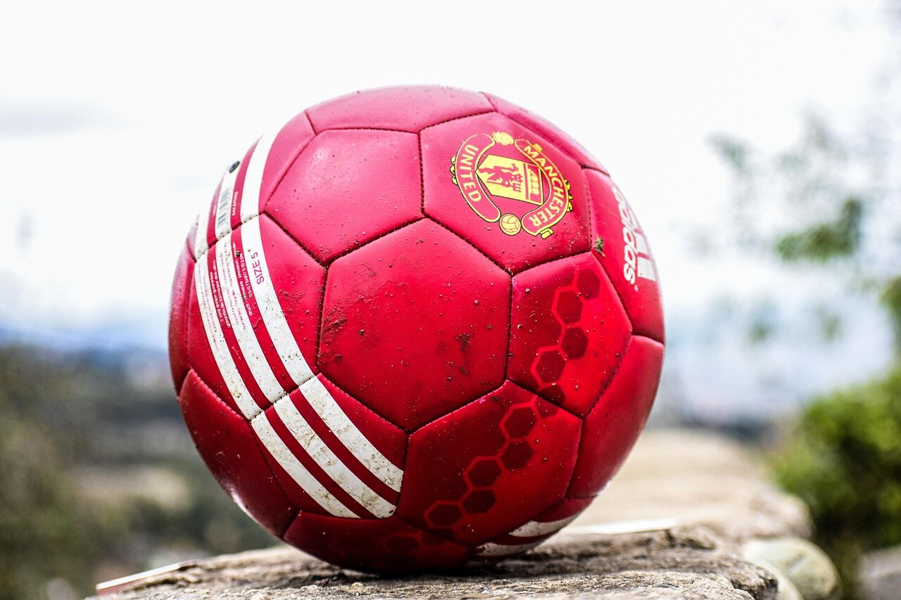 Fans gather in a stadium, eagerly watching a tense moment during a crucial football match as players compete for possession of the ball.